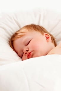 Lille dreng der sover i hvidt sengetøj